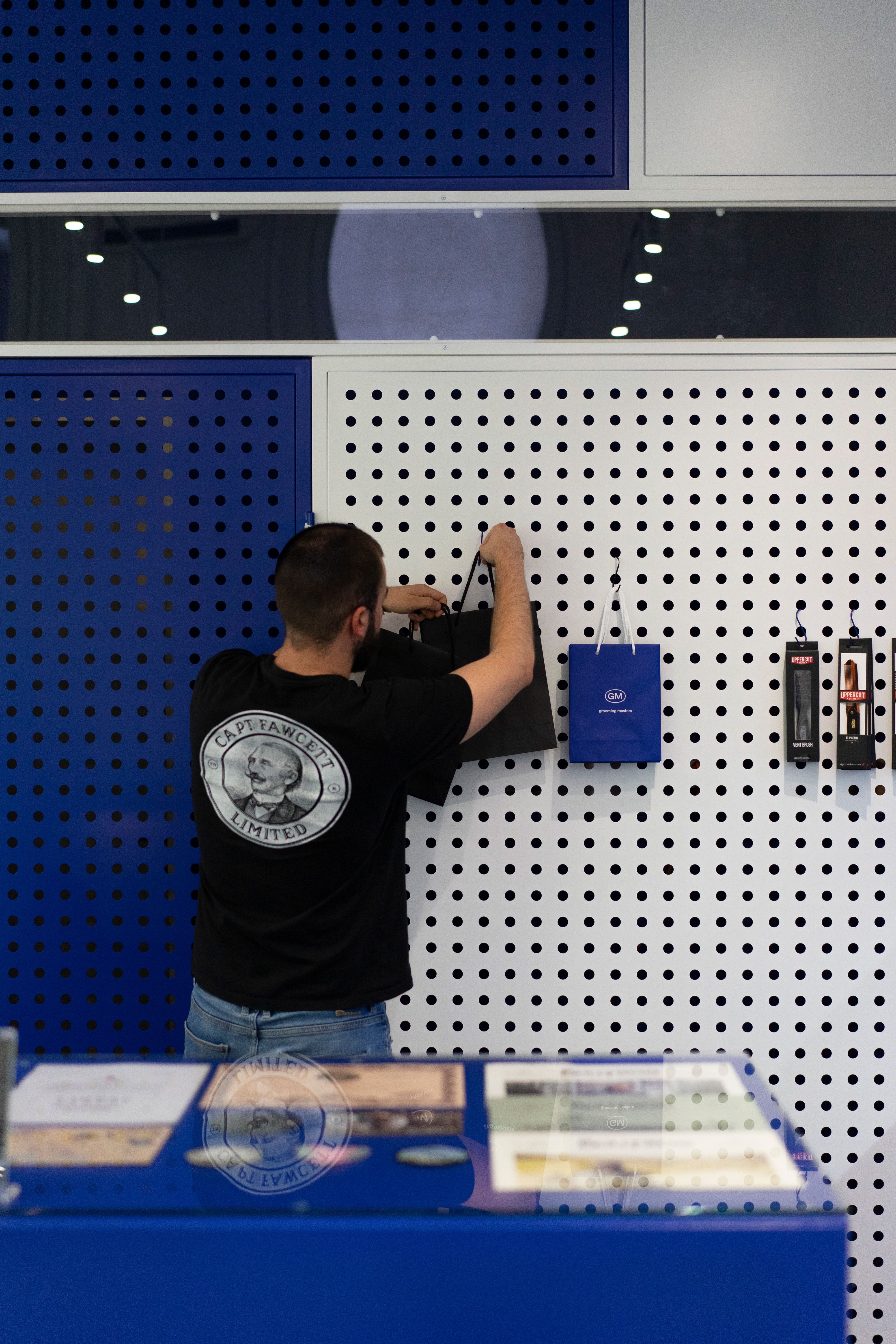 A staff member hanging Grooming Masters paper bags on the pegboard wall behind the counter at The Embassy