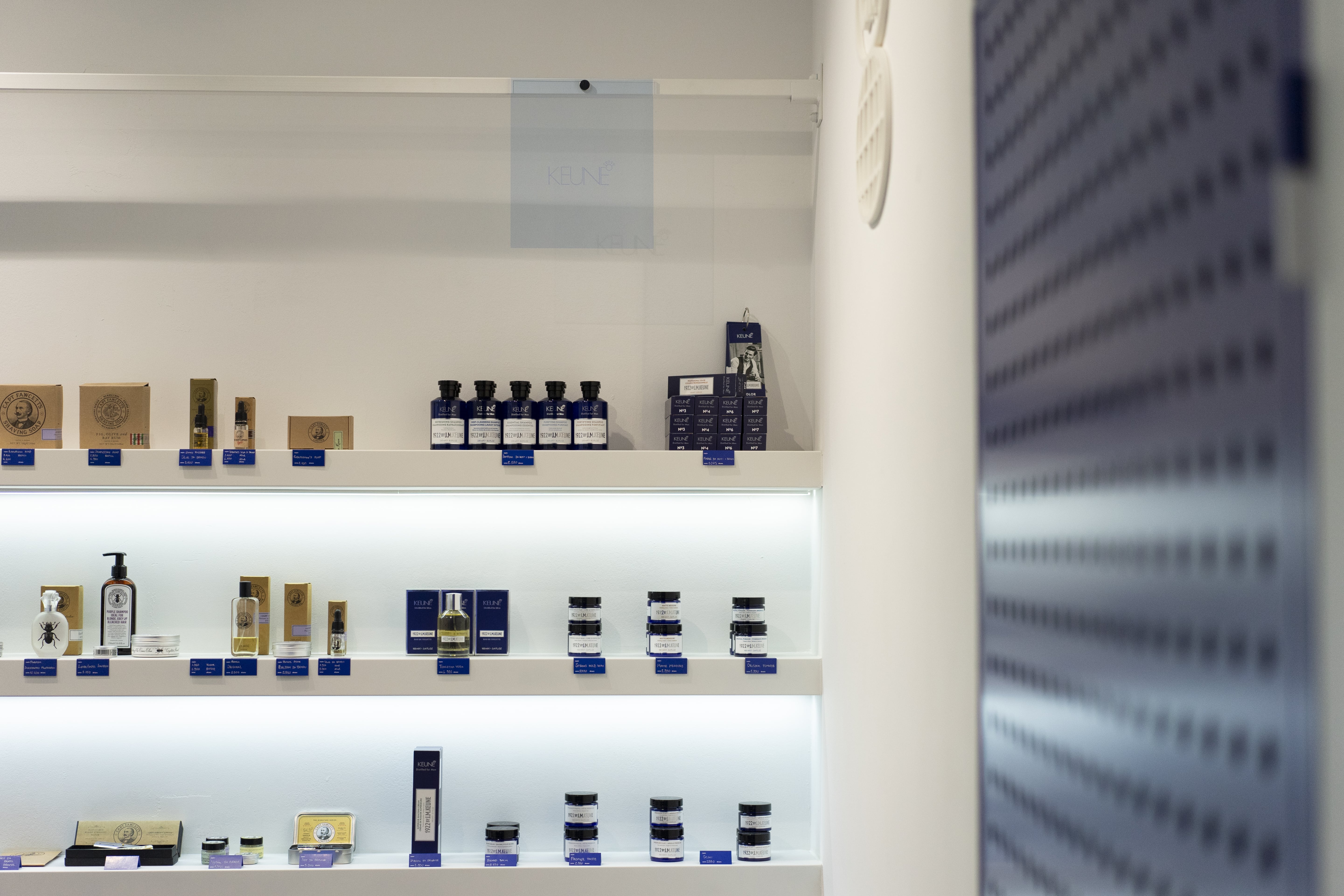 Backlit white shelving — Captain Fawcett and Keune 1922 ranges under strip light