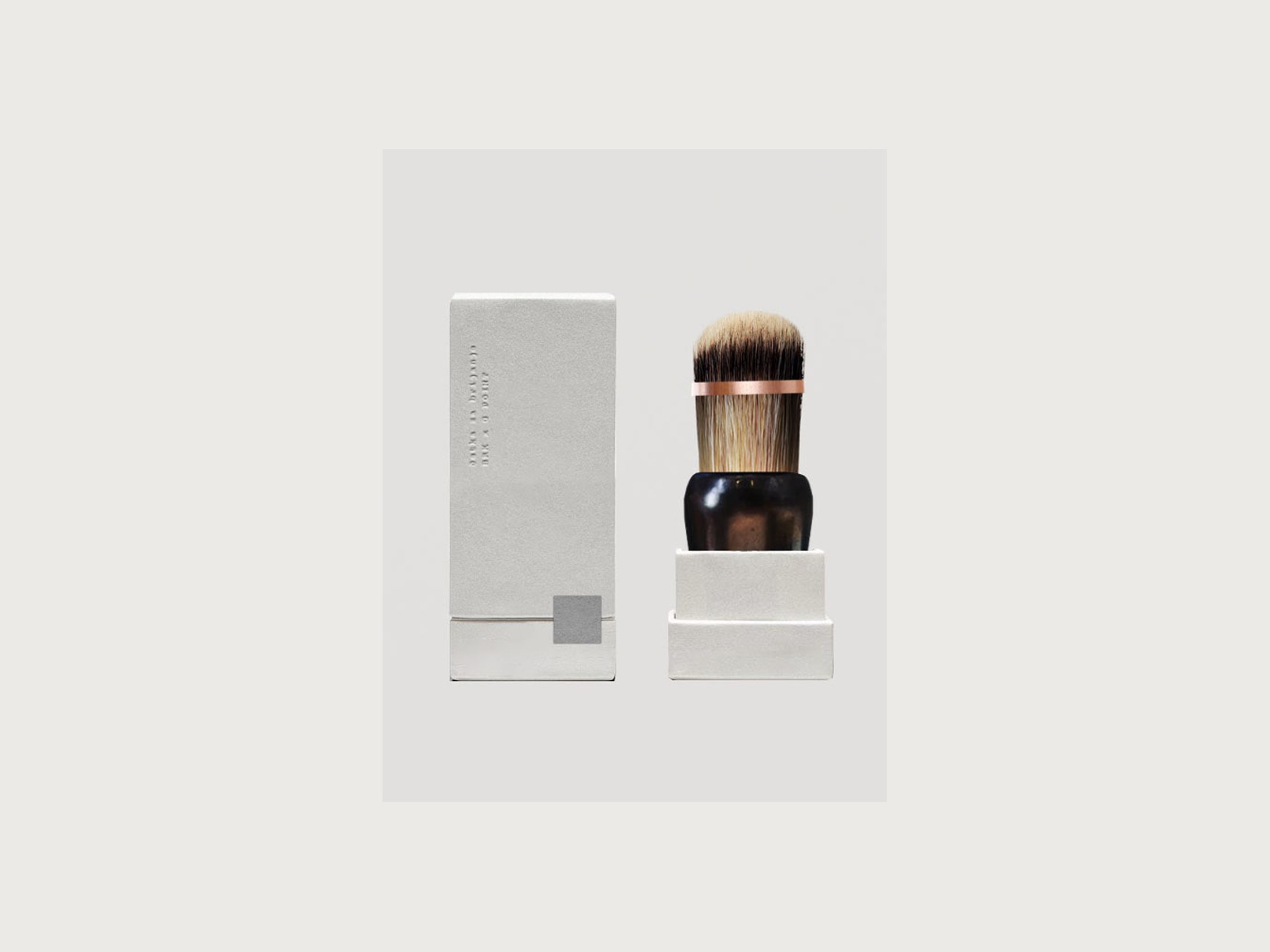 Shaving brush with a dark horn handle and copper band, standing in its embossed white box