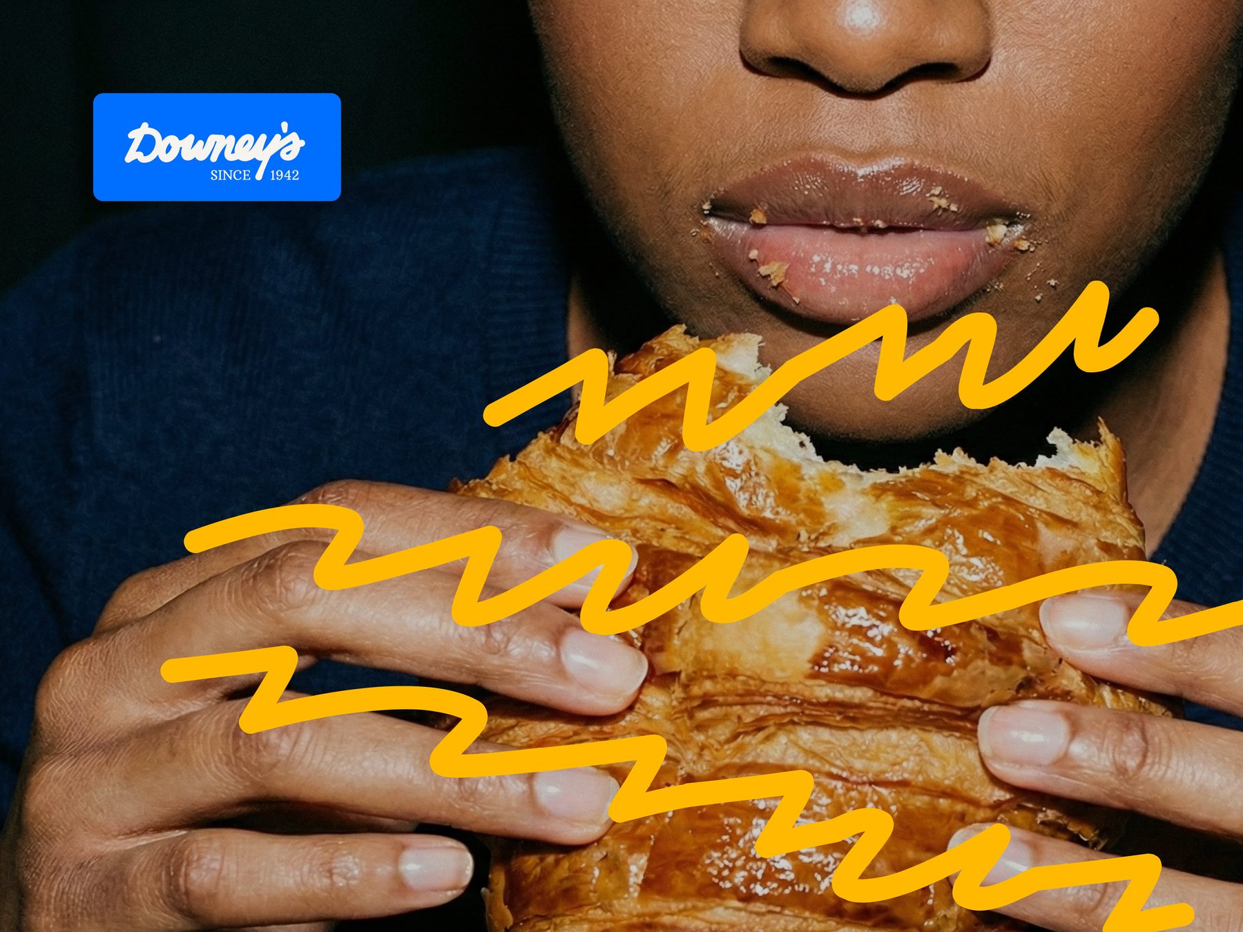 Campaign photo: biting into a croissant, brand squiggles scribbled over the pastry