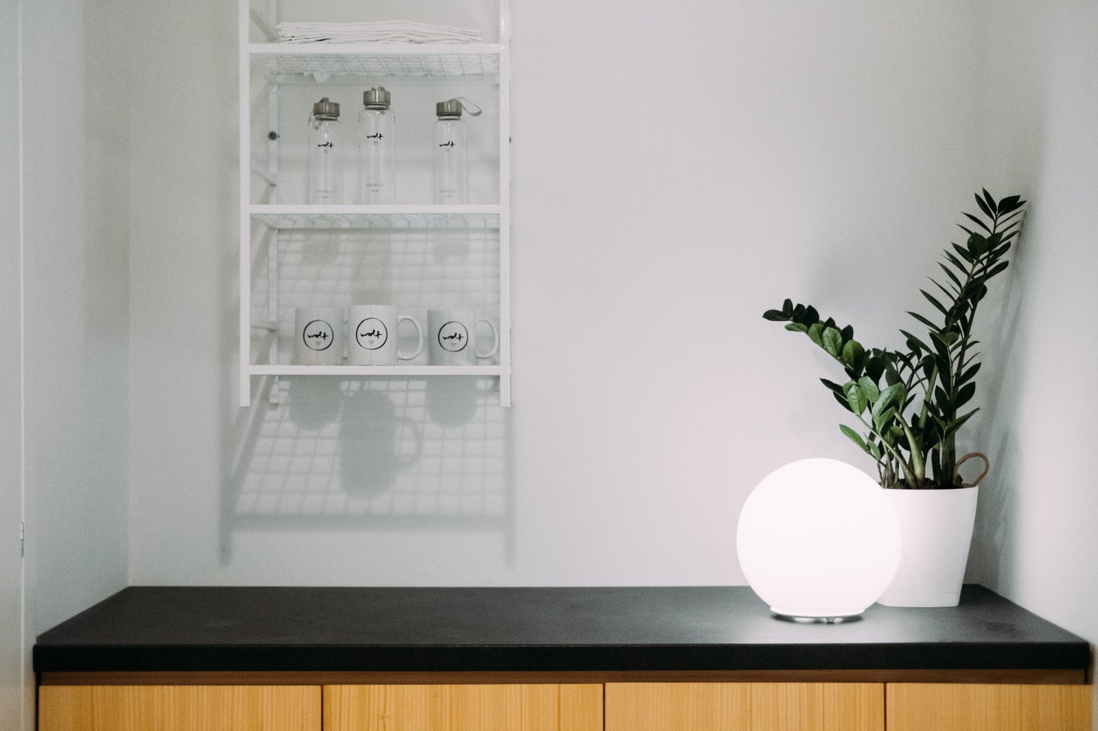 The merch wall — bottles and mugs on a white wire shelf above wood cabinets, globe lamp glowing